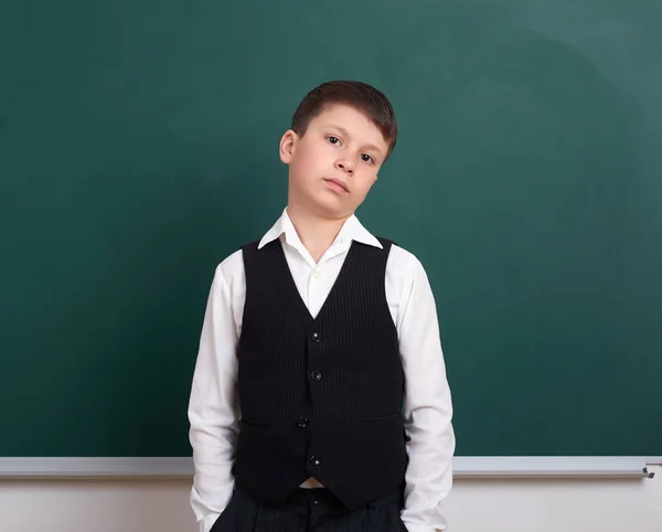 Indifferent school boy portrait near green blank chalkboard background, dressed in classic suit, one pupil, education concept — Stock Photo, Image