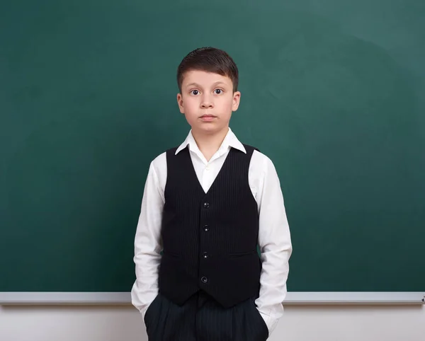 Indifferent school boy portrait near green blank chalkboard background, dressed in classic suit, one pupil, education concept — Stock Photo, Image