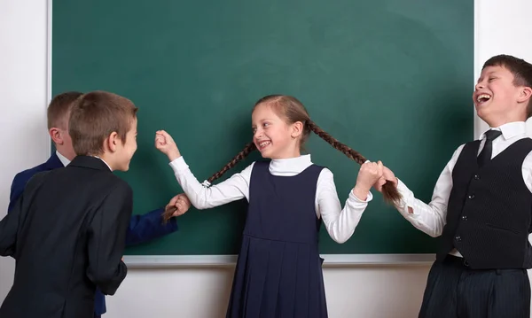 Child play and having fun, boys pull the girl braids, near blank school chalkboard background, dressed in classic black suit, group pupil, education concept — Stock Photo, Image