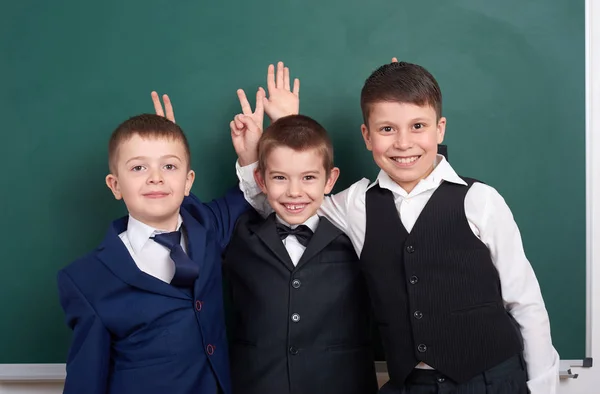 Basisschool jongen vrienden, gek rond in de buurt van leeg schoolbord achtergrond, gekleed in een klassieke zwarte pak, groep leerling, onderwijs en vriendschap concept — Stockfoto