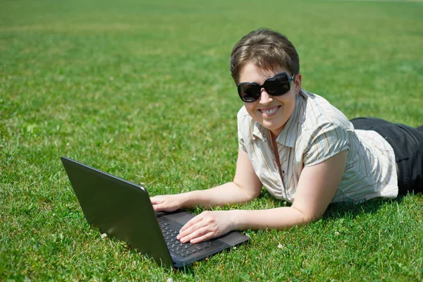 Frau arbeitet im Sommer am Laptop im Freien, auf dem Bauch auf der grünen Wiese liegen, glückliche Menschen, Stadtpark — Stockfoto