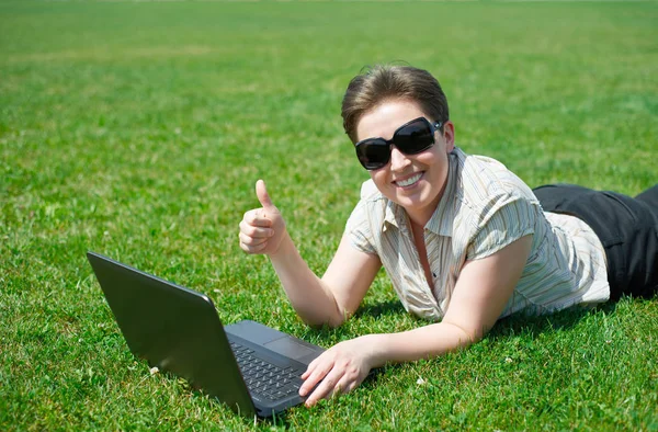 Frau arbeitet im Sommer am Laptop im Freien, auf dem Bauch auf der grünen Wiese liegen, beste Geste zeigen, glückliche Menschen, Stadtpark — Stockfoto