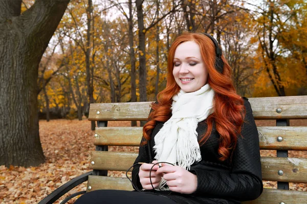 年轻女子肖像在秋天的公园，在耳机上听音乐 — 图库照片