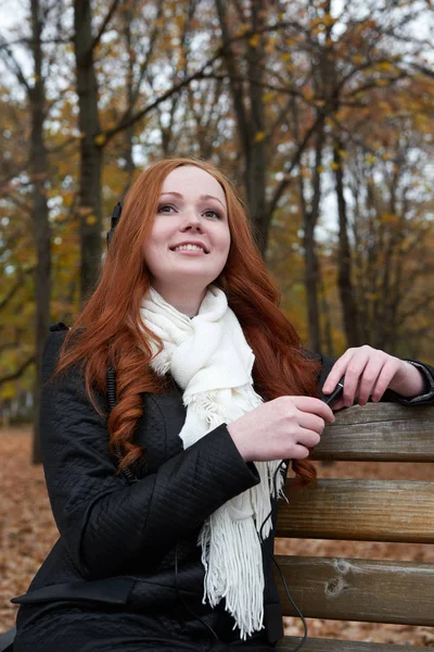 Young woman portrait in autumn park, listening to music on headphones — Stock Photo, Image