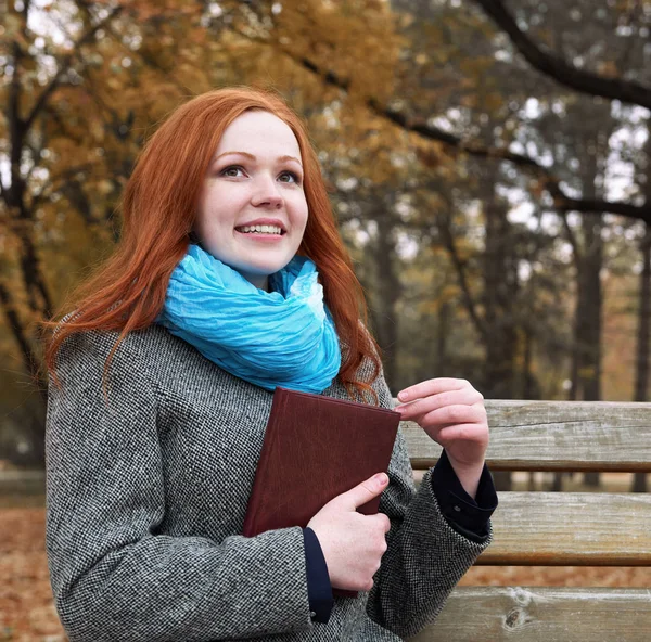 Redhead girl with book in autumn park, yellow leaves and trees — Stock Photo, Image
