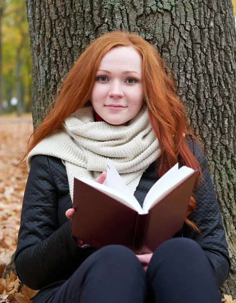 Young woman sit near tree in autumn park and read book, yellow leaves — Stock Photo, Image