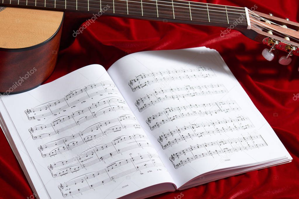 acoustic guitar and music notes on red velvet fabric, close view of objects