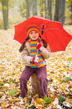 çocuk kız sit sonbahar ormandaki, düşen yapraklar arka plan üzerinde kırmızı şemsiye ile gövde üzerinde sonbahar sezon
