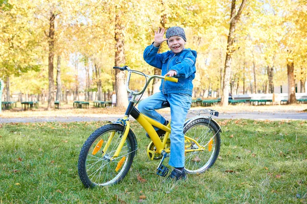 Хлопчик їде на велосипеді в осінньому парку, яскравий сонячний день, падає листя на фоні — стокове фото