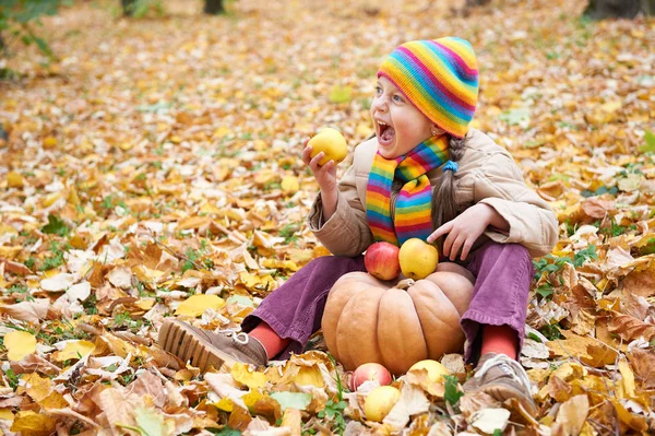 Kind isst Apfel und Kürbis im Wald, sitzt auf Herbstblättern im Hintergrund, Herbstzeit — Stockfoto