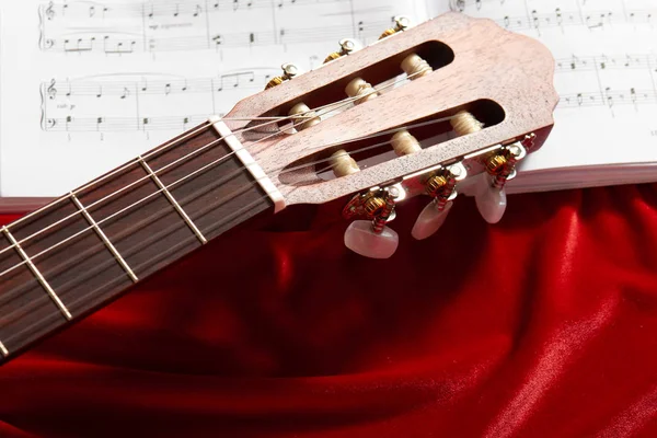 acoustic guitar and music notes on red velvet fabric, close view of objects