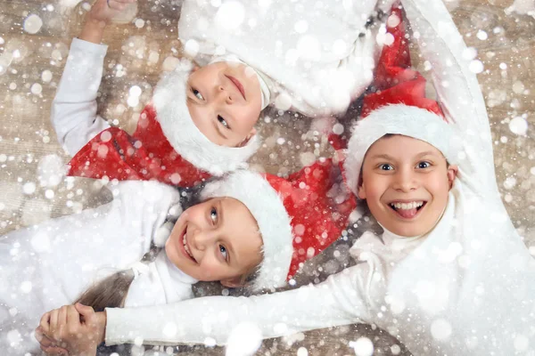 Щаслива дитина тримає руки і лежить на дерев'яному фоні, одягнений у різдвяний капелюх Санта і весело, концепція зимових свят, прикраса снігу — стокове фото
