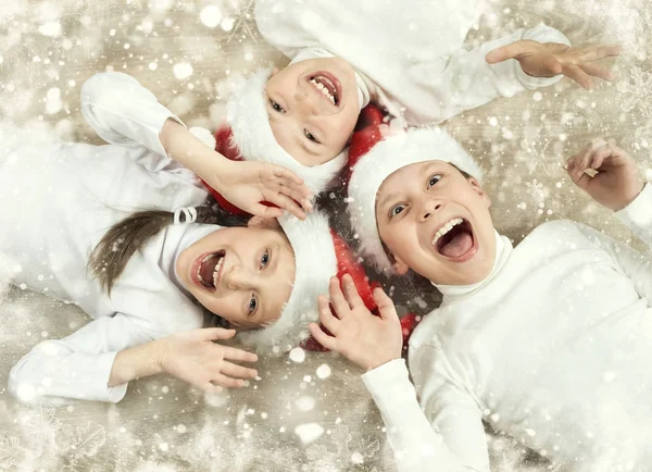 Счастливый ребенок, лежащий вместе на деревянном фоне, одетый в рождественскую шляпу Санта-Клауса и веселясь, зимний праздник концепция, снежное оформление, желтый тонированный — стоковое фото