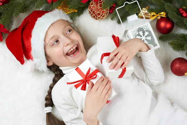 Menina criança mentir na decoração de Natal na pele branca, close-up rosto, vestido com chapéu de santa, conceito de férias de inverno, árvore de xmas — Fotografia de Stock