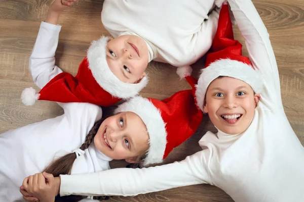 Niño feliz cogido de la mano y acostado sobre fondo de madera, vestido con sombrero de Navidad de Santa y divertirse, concepto de vacaciones de invierno — Foto de Stock