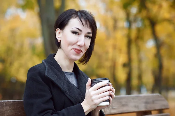 Mädchen mit Kaffee auf Bank sitzend, Herbstzeit, Stadtpark, gelbe Blätter — Stockfoto