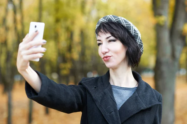 Девушка фотографирует по телефону в осеннем городском парке, желтые листья и деревья, осенний сезон — стоковое фото
