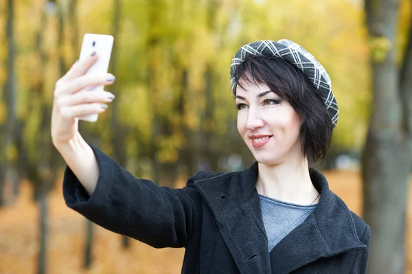 Девушка фотографирует по телефону в осеннем городском парке, желтые листья и деревья, осенний сезон — стоковое фото