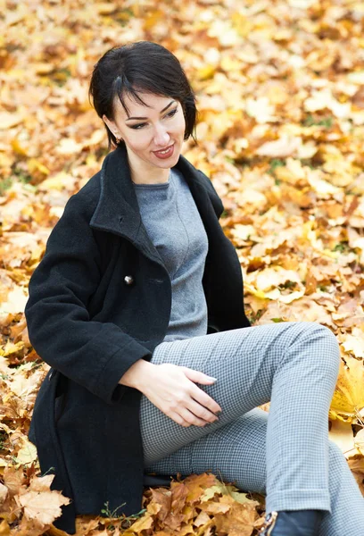 Meisje in zwarte jas, zittend op een gele bladeren in de herfst stadspark, val seizoen — Stockfoto