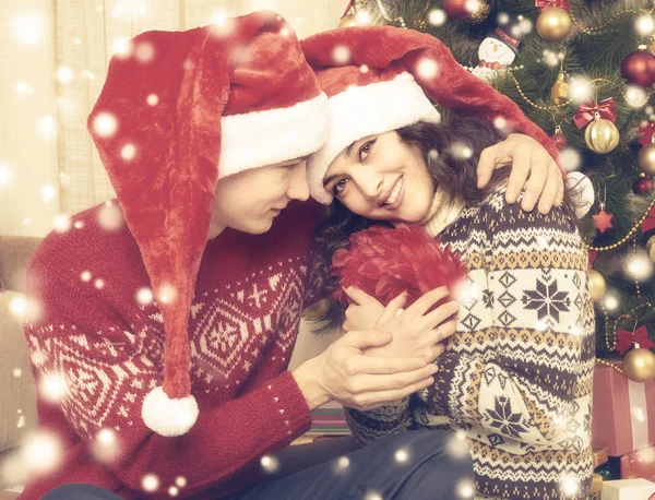 Casal feliz abraçar perto de árvore de natal e decoração em casa. férias de inverno e conceito de amor. Amarelo tonificado com neve . — Fotografia de Stock