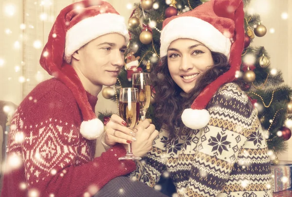 La coppia felice con bicchiere di champagne si siede vicino all'albero di Natale a casa. Vacanza invernale e concetto di amore. Giallo tonico con neve . — Foto Stock