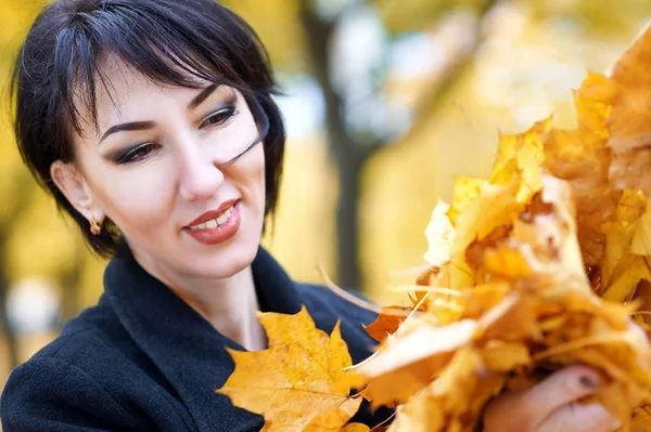 Beautiful woman face closeup with handful of yellow leaves in autumn outdoor, trees on background, fall season — Stock Photo, Image