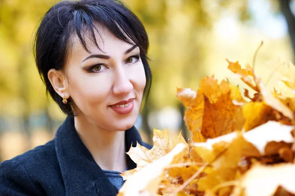 Schöne Frau Gesicht Nahaufnahme mit einer Handvoll gelber Blätter im Herbst im Freien, Bäume auf dem Hintergrund, Herbstsaison — Stockfoto