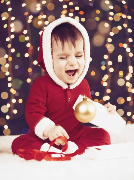 Маленький мальчик, одетый как Санта играть с рождественским украшением, темный фон с освещением и boke огни, зимний праздник концепции — стоковое фото