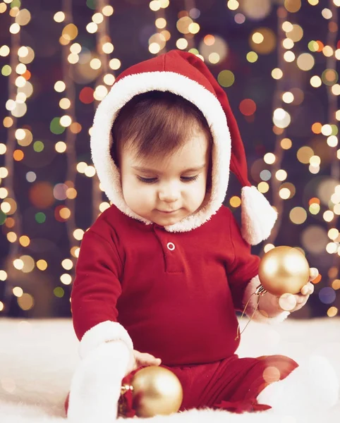 Niño pequeño vestido de santa jugando con la decoración de Navidad, fondo oscuro con iluminación y luces de arco, concepto de vacaciones de invierno — Foto de Stock