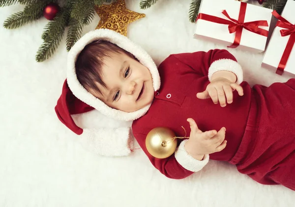 Little child boy dressed as santa playing with christmas decoration, lie on white fur, winter holiday concept — Stock Photo, Image