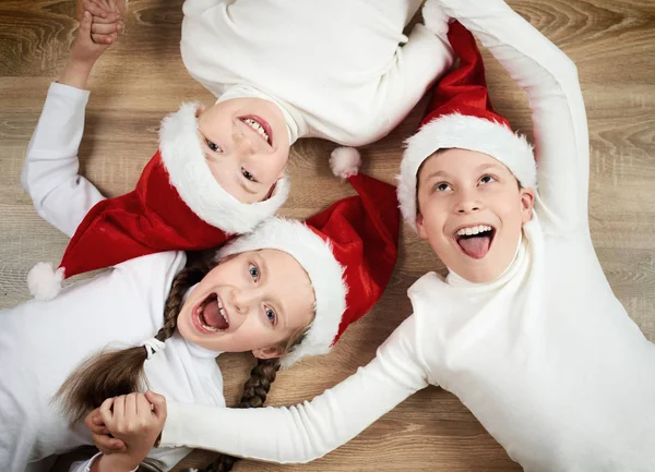 Criança feliz deitada em conjunto no fundo de madeira, vestida com chapéu de Natal Santa e se divertindo, feliz ano novo e conceito de férias de inverno — Fotografia de Stock