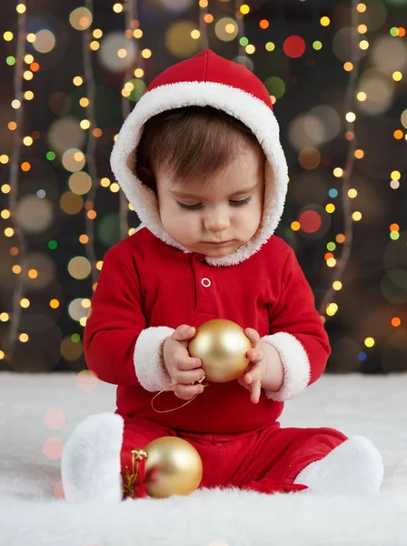 Малыш, одетый как Санта, играет с рождественскими игрушками, темный фон с подсветкой, счастливого нового года и зимних каникул — стоковое фото