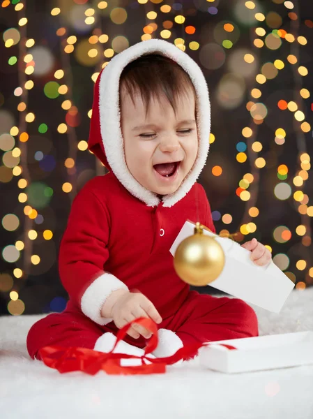 Малыш, одетый как Санта, играет с рождественскими игрушками, темный фон с подсветкой, счастливого нового года и зимних каникул — стоковое фото