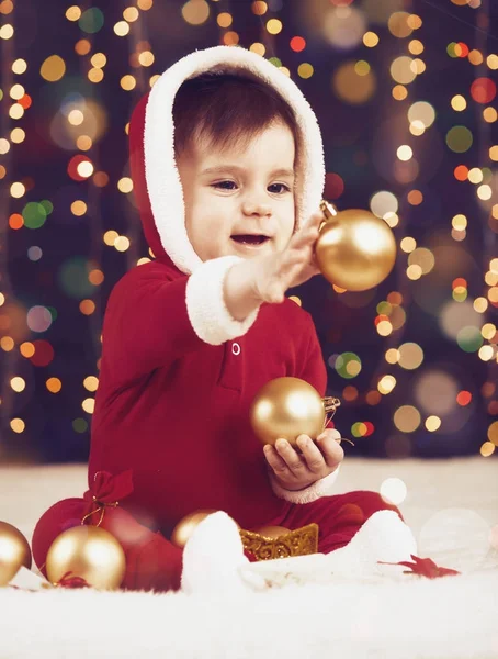 Niño pequeño vestido de santa jugando con la decoración de Navidad, fondo oscuro con iluminación y luces de arco, concepto de vacaciones de invierno — Foto de Stock
