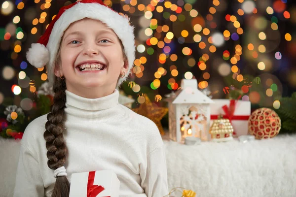 Menina criança vestida com chapéu de Papai Noel com presentes de Natal no fundo iluminado escuro, feliz ano novo e conceito de celebração de inverno — Fotografia de Stock