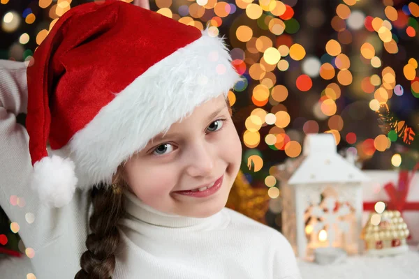 Menina criança vestida com chapéu de Papai Noel com presentes de Natal no fundo iluminado escuro, feliz ano novo e conceito de celebração de inverno — Fotografia de Stock