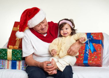 Büyükanne ve torunu hediye kutuları ile santa şapka giymiş, beyaz arka plan oturun. Yeni yıl arifesi ve Noel tatil kavramı.