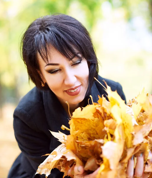 Mooie vrouw portret met handvol bladeren in de herfst buiten, gele bladeren en bomen op de achtergrond, vallen seizoen — Stockfoto