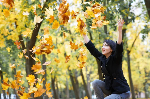 美丽的妇女投掷叶子在秋天室外, 黄色叶子和树在背景, 秋天季节 — 图库照片