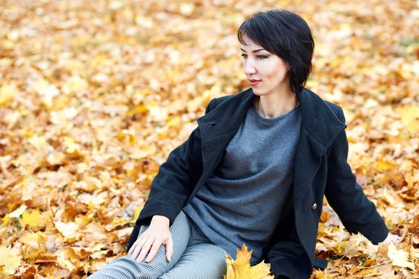 Bela mulher sentar no outono ao ar livre, folhas amarelas e árvores no fundo, temporada de outono — Fotografia de Stock