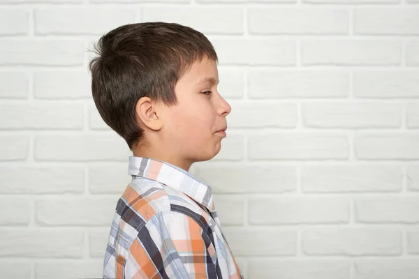 Portrait of a emotional boy standing near white brick wall, dressed in a plaid shirt — Stock Photo, Image