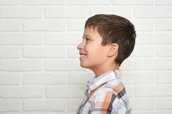 Retrato de um menino emocional em pé perto da parede de tijolo branco, vestido com uma camisa xadrez — Fotografia de Stock