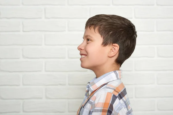 Portrait of a emotional boy standing near white brick wall, dressed in a plaid shirt — Stock Photo, Image