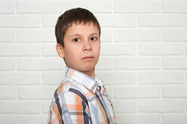 Portrait of a emotional boy standing near white brick wall, dressed in a plaid shirt — Stock Photo, Image