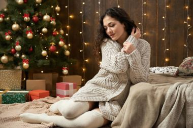 genç kız Noel ışıkları ve Dekorasyon, giyinmiş beyaz kazak ve çorap, koyu ahşap arka plan, kış tatil kavramı üzerinde köknar ağacı