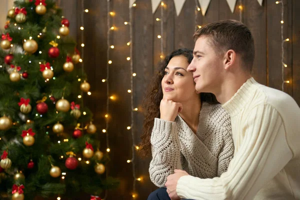 Coppia in luci di Natale e decorazione, vestito di bianco, giovane ragazza e uomo, abete su sfondo di legno scuro, concetto di vacanza invernale — Foto Stock