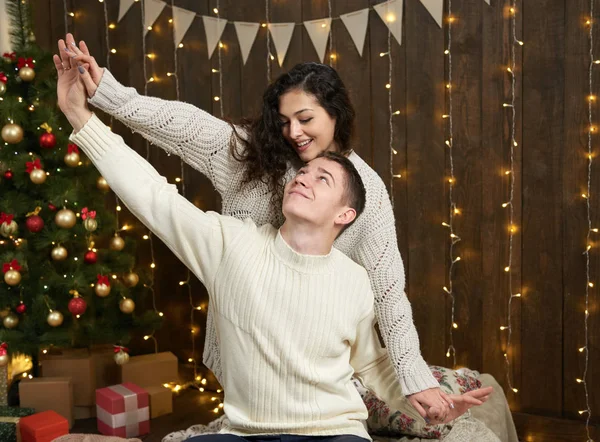 Coppia in luci di Natale e decorazione, vestito di bianco, giovane ragazza e uomo, abete su sfondo di legno scuro, concetto di vacanza invernale — Foto Stock