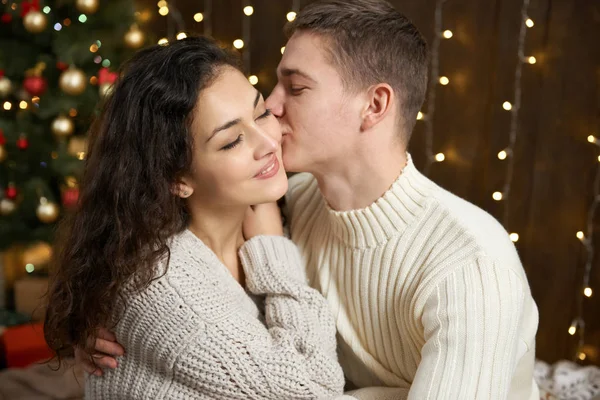 Пара в різдвяних вогнях і прикрасах, одягнена в біле, молода дівчина і чоловік, ялинка на темному дерев'яному фоні, концепція зимового свята — стокове фото