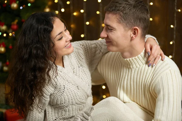 Paar in Kerstverlichting en decoratie, gekleed in wit, jong meisje en man, fir tree op donkere houten achtergrond, concept van winter vakantie — Stockfoto