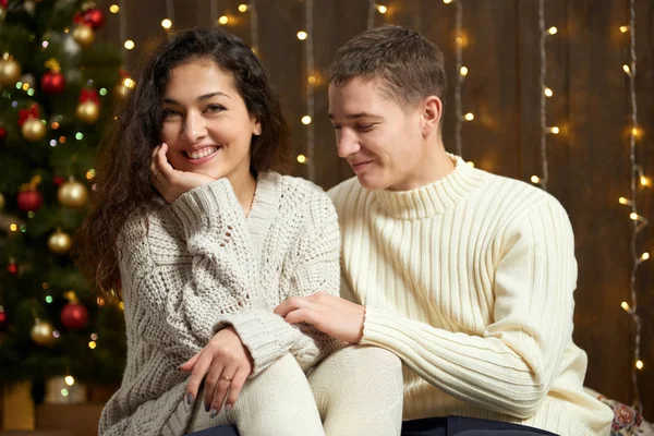 Coppia in luci di Natale e decorazione, vestito di bianco, giovane ragazza e uomo, abete su sfondo di legno scuro, concetto di vacanza invernale — Foto Stock